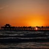 Beautiful sunset over the ocean with a pier and silhouetted people.