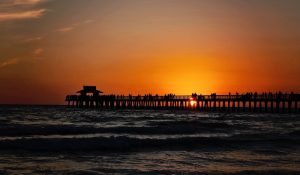 Beautiful sunset over the ocean with a pier and silhouetted people.